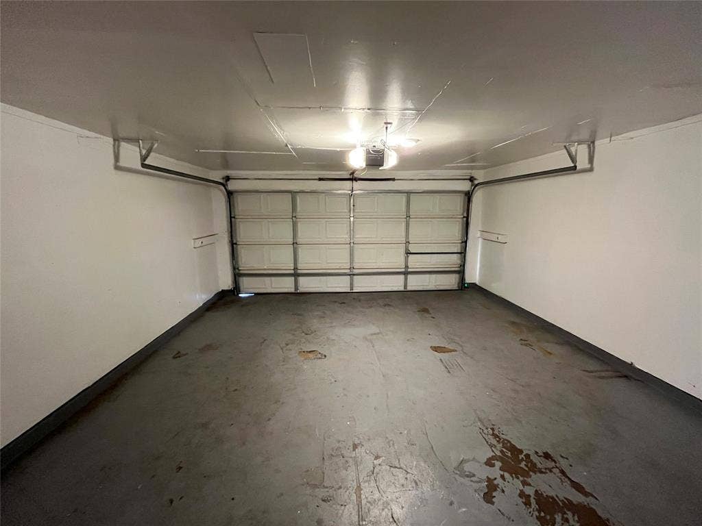 1843 Greendale Drive, Dallas, TX 75217 Attached garage with an overhead door, smooth white walls, and a concrete floor