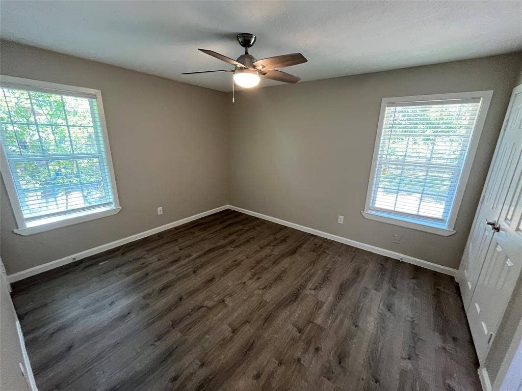 1843 Greendale Drive, Dallas, TX 75217 Wood-finish flooring, neutral wall tones, two large windows with blinds, a ceiling fan with integrated lighting, and a white paneled door