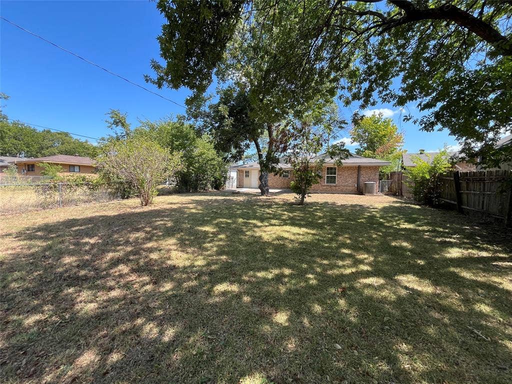 1843 Greendale Drive, Dallas, TX 75217 Expansive backyard with a manicured lawn, established trees, and a brick exterior building