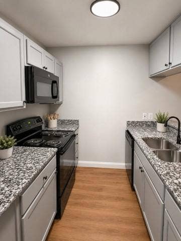 624 E 3rd Street, #202, Springtown, TX 76082 Galley kitchen featuring light gray cabinetry, black appliances, speckled countertops, stainless steel double basin sink, and wood-finish flooring