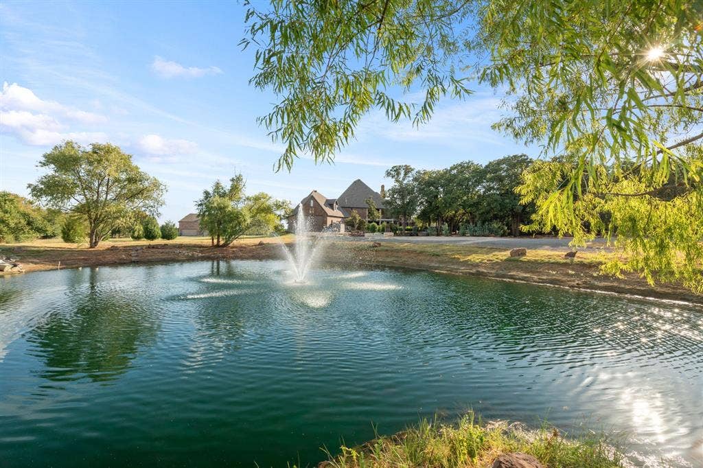 Expansive pond with a central fountain, stocked with fish and surrounded by mature trees and natural landscaping