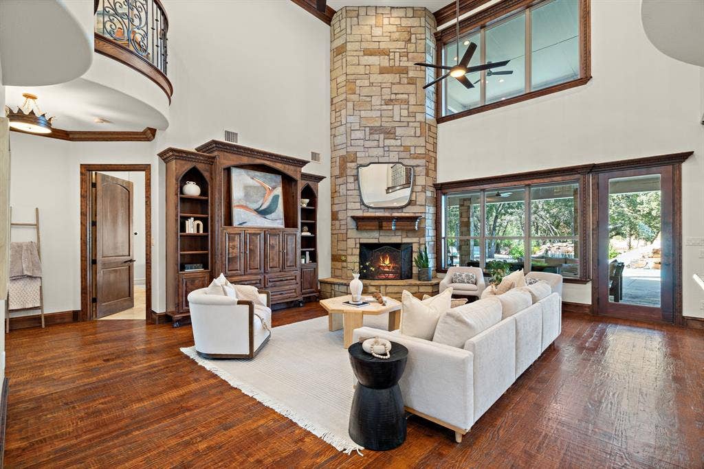 Vaulted ceilings with an exposed wood beam, a floor-to-ceiling stacked stone fireplace, wood-finish flooring, and a built-in entertainment center with integrated shelving