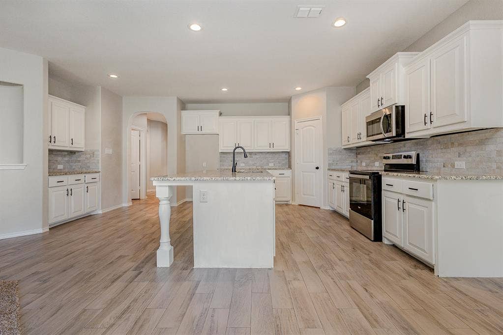 928 Dove Cove, Argyle, TX 76226 View of kitchen from living and dining area. Featuring white cabinets, large island with sink and sitting area, dry bar that may be used as coffee bar, stainless steel appliances