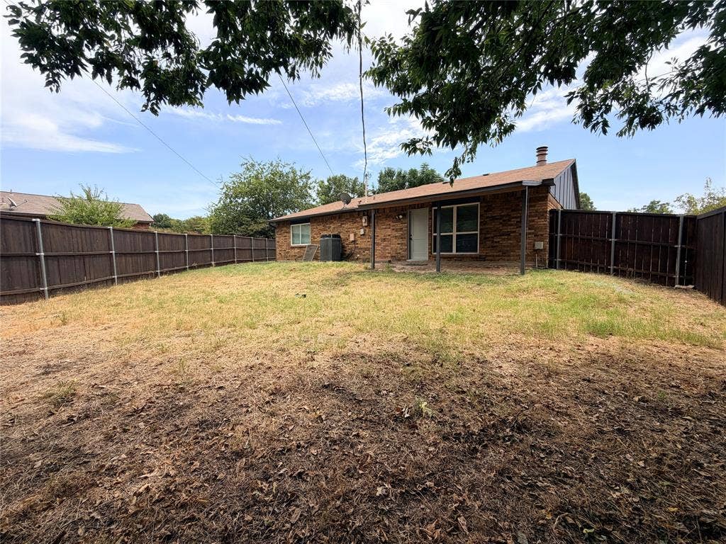 Brick exterior with an attached covered patio, a fenced yard, and a pitched roof