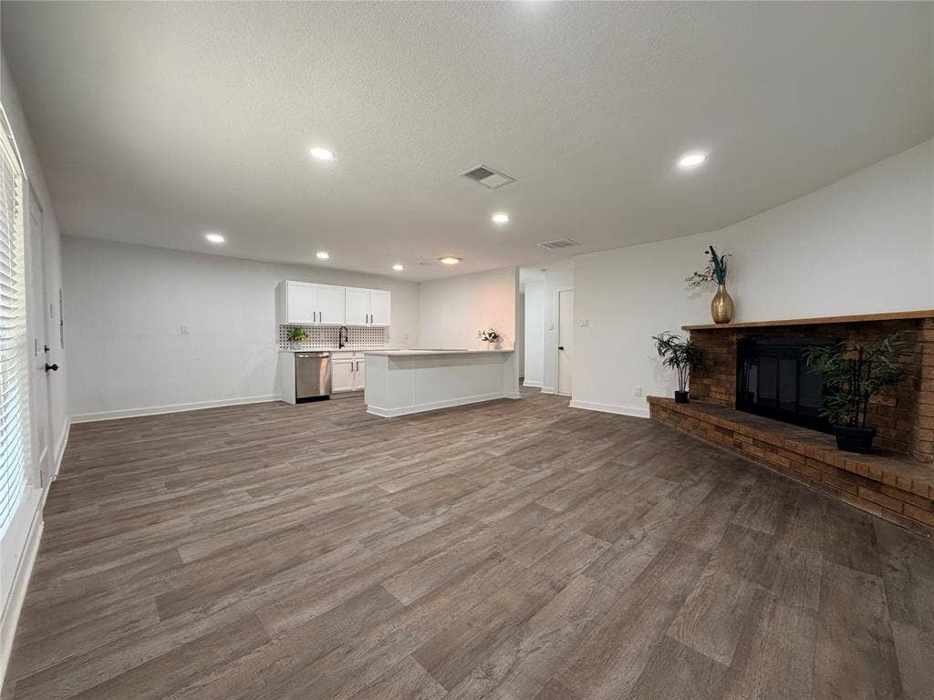 Open-concept living area featuring wood-finish flooring, recessed lighting, and a brick-surround fireplace