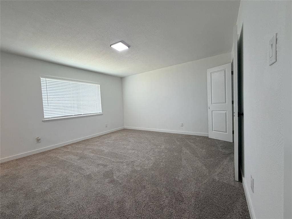 Expansive room featuring neutral-toned carpeting, a window with horizontal blinds, and a flush-mount ceiling light fixture