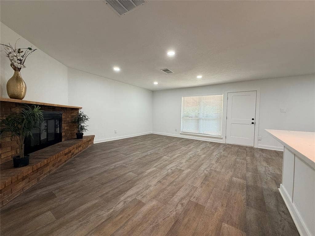Spacious room with wood-finish flooring, recessed lighting, a brick fireplace, and a large window with blinds