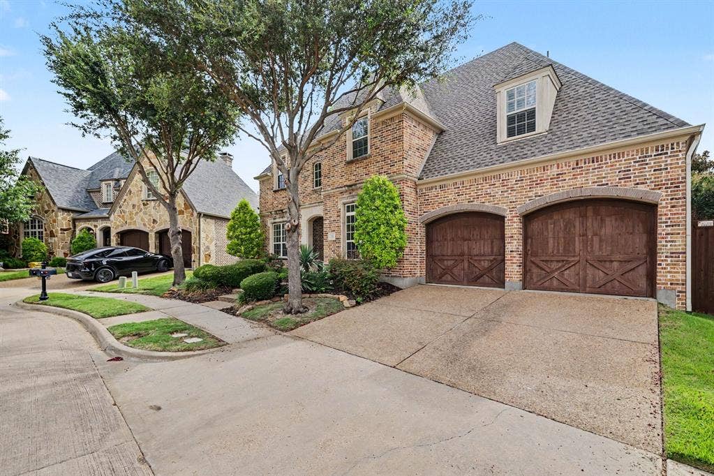 408 Blue Ridge Court, Allen, TX 75013 Brick exterior with stone accents, two arched wood-finish garage doors, concrete driveway, and dormer windows