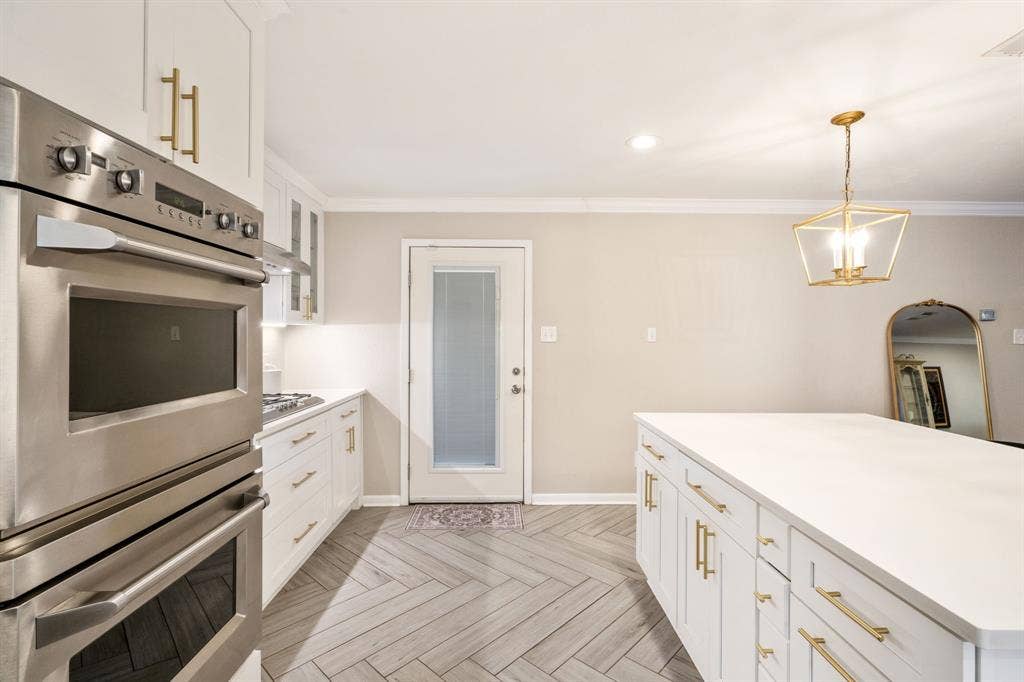 2711 Alco Avenue, Dallas, TX 75211 Gourmet kitchen featuring stainless steel double ovens, white cabinetry with brass hardware, and a center island with a solid surface countertop