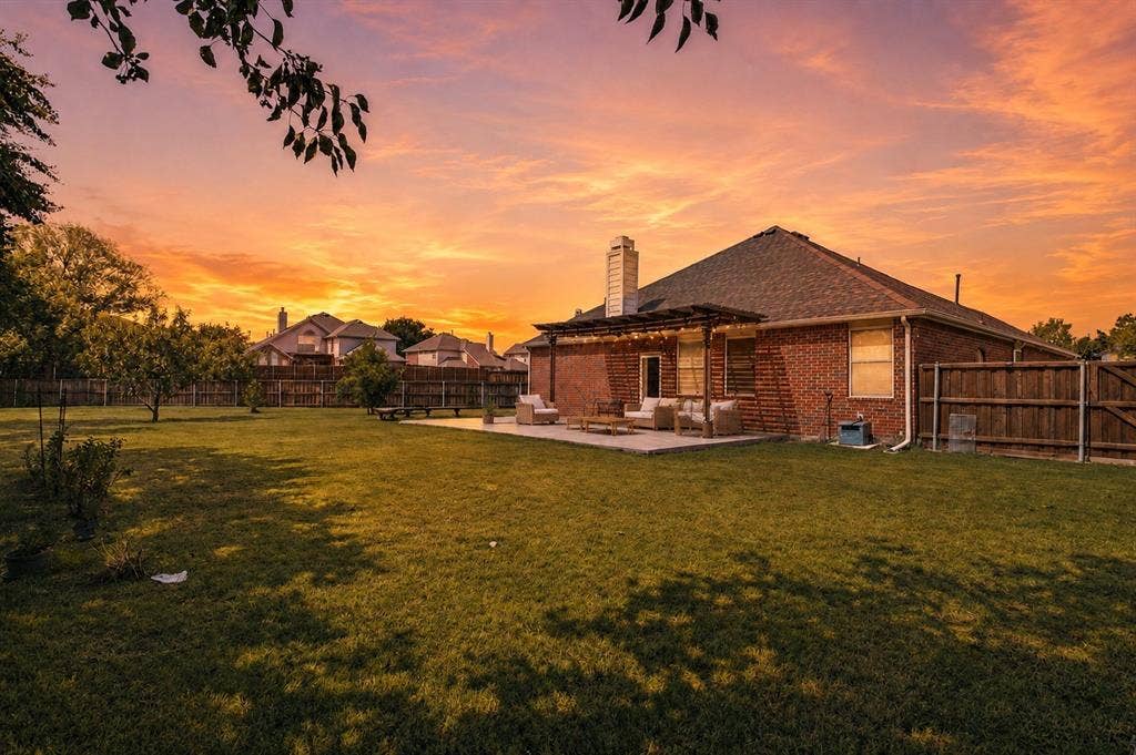 9604 Bull Creek Drive, Plano, TX 75025 Expansive backyard featuring a manicured lawn, mature trees, and a concrete patio with an attached pergola