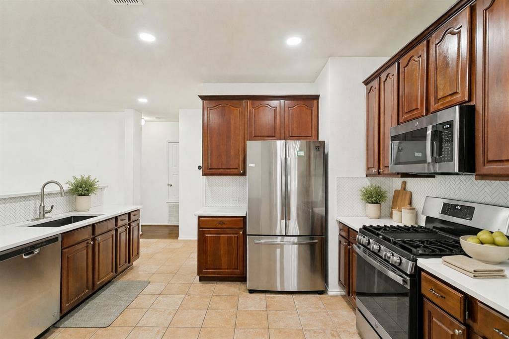 9604 Bull Creek Drive, Plano, TX 75025 Kitchen featuring stainless steel appliances, wood cabinetry, light countertops, and a herringbone tile backsplash