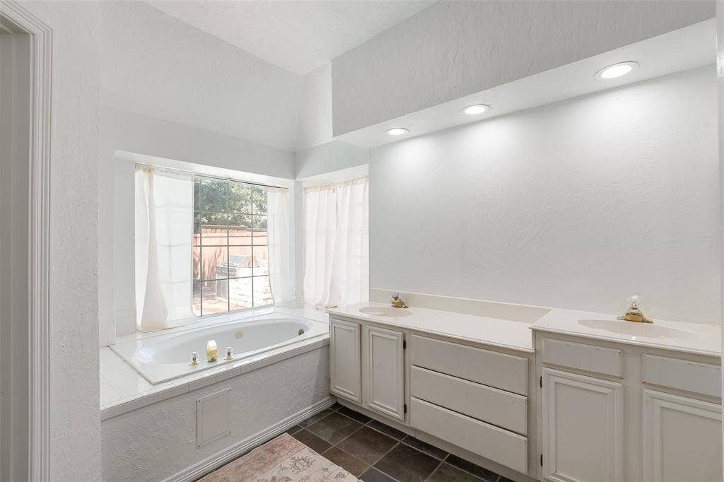 Spacious bathroom with an integrated soaking tub, dual vanity with solid surface countertops, recessed lighting, and dark tile flooring