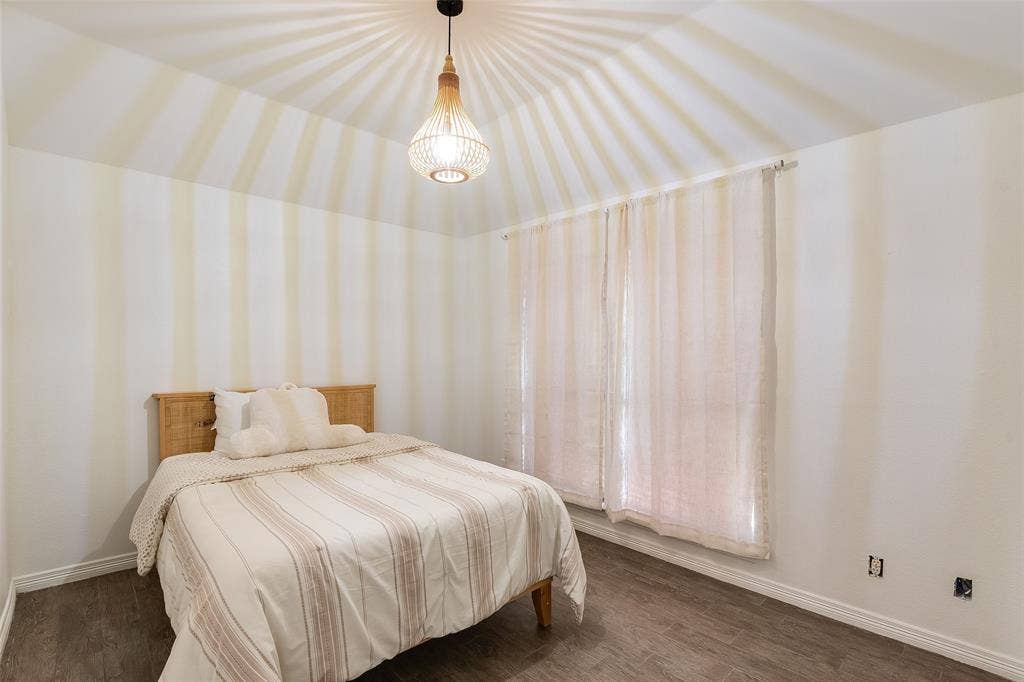 Vaulted ceiling featuring a decorative pendant light fixture, wood-finish flooring, and window with sheer curtains