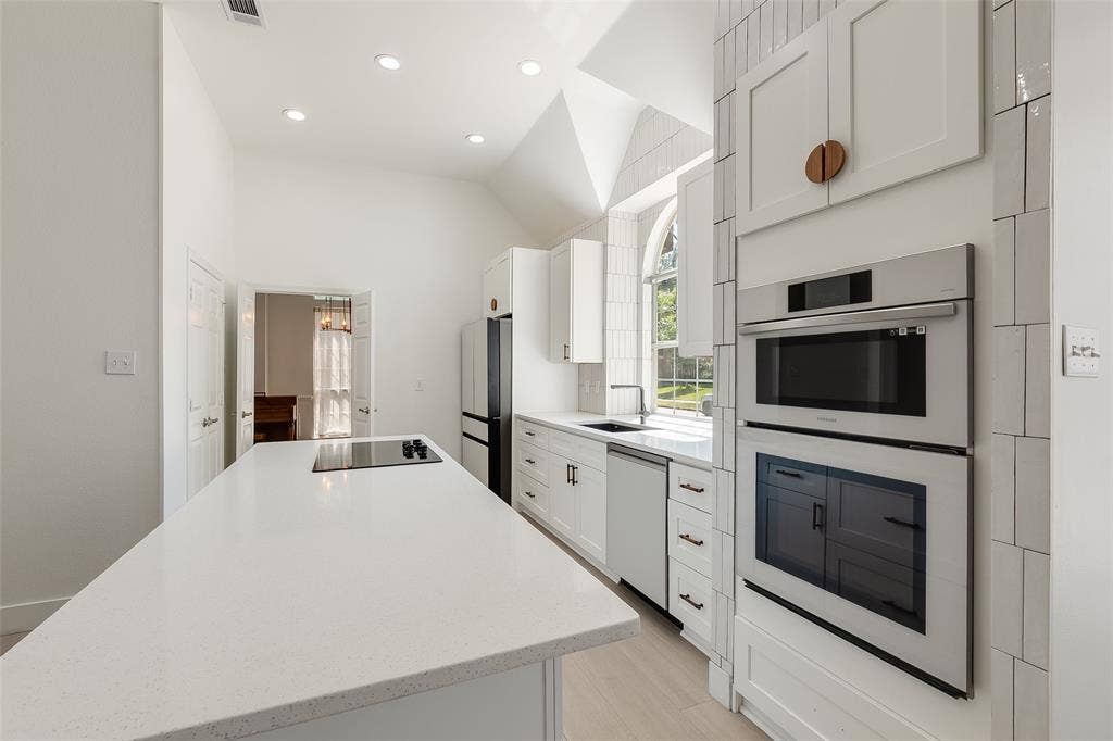 Contemporary kitchen featuring a vaulted ceiling, recessed lighting, white cabinetry, integrated stainless steel appliances, and a central island with a cooktop