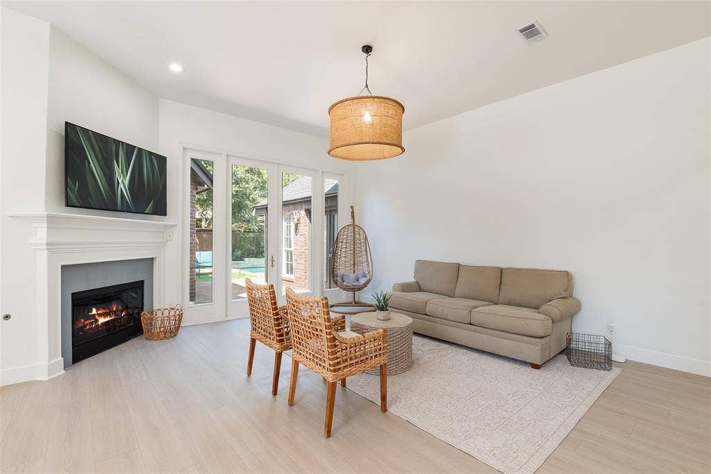 White walls, fireplace with mantel, recessed lighting, wood-finish flooring, and glass-paneled doors