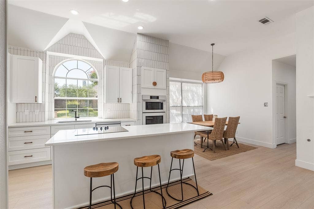 Bright kitchen with vaulted ceiling, arched window, white cabinetry, integrated cooktop, and built-in double oven