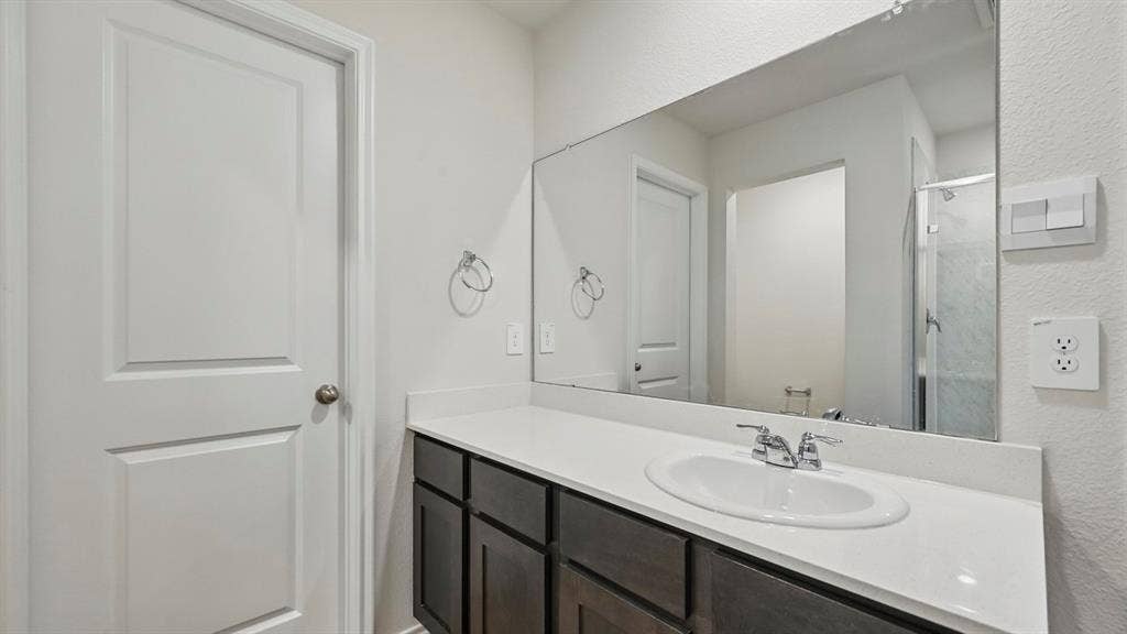 1912 Freeman Street, Tyler, TX 75702 Bathroom featuring a single vanity with dark wood-finish cabinetry, a white countertop, an undermount sink with a chrome faucet, and a large wall-mounted mirror