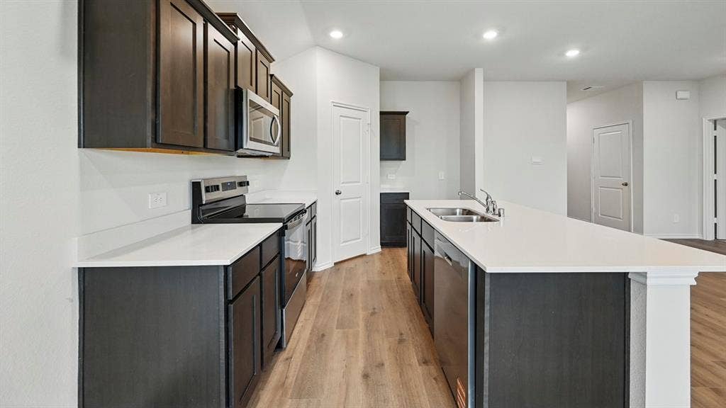 1912 Freeman Street, Tyler, TX 75702 Spacious kitchen featuring dark wood cabinetry, light countertops, stainless steel appliances, a large island with an integrated sink, and wood-finish flooring