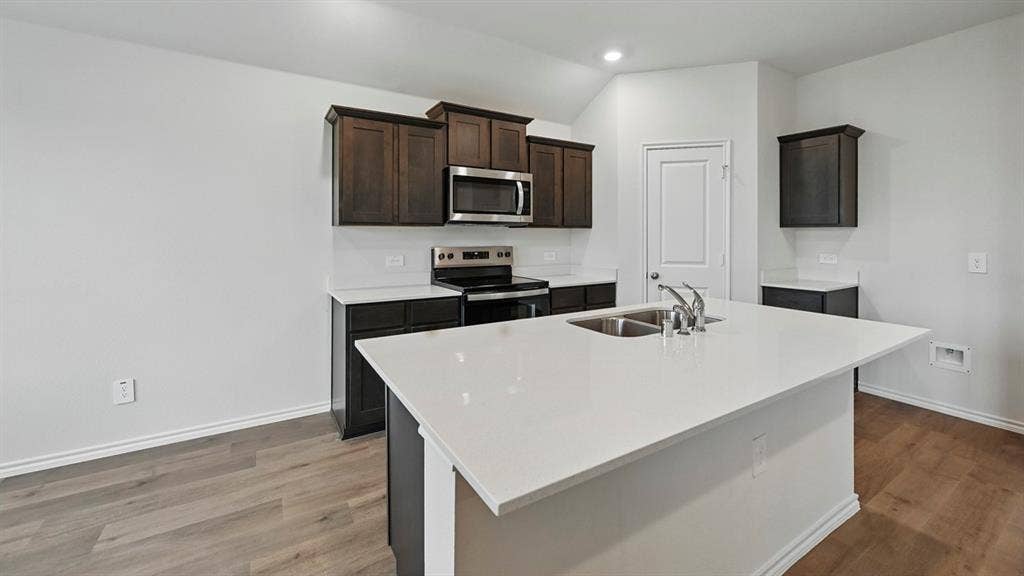 1912 Freeman Street, Tyler, TX 75702 Kitchen featuring wood-finish flooring, dark wood-finish cabinetry, stainless steel appliances, white countertops, and an island with an undermount double sink