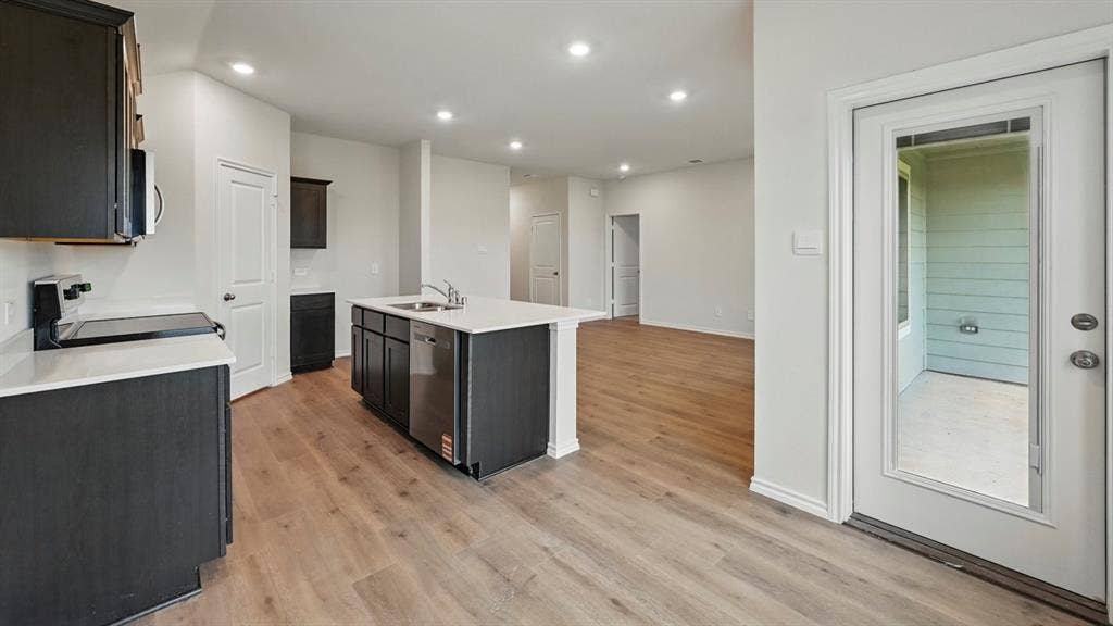 1912 Freeman Street, Tyler, TX 75702 Kitchen featuring a central island with sink, stainless steel dishwasher, dark wood-finish cabinetry, and light-toned countertops