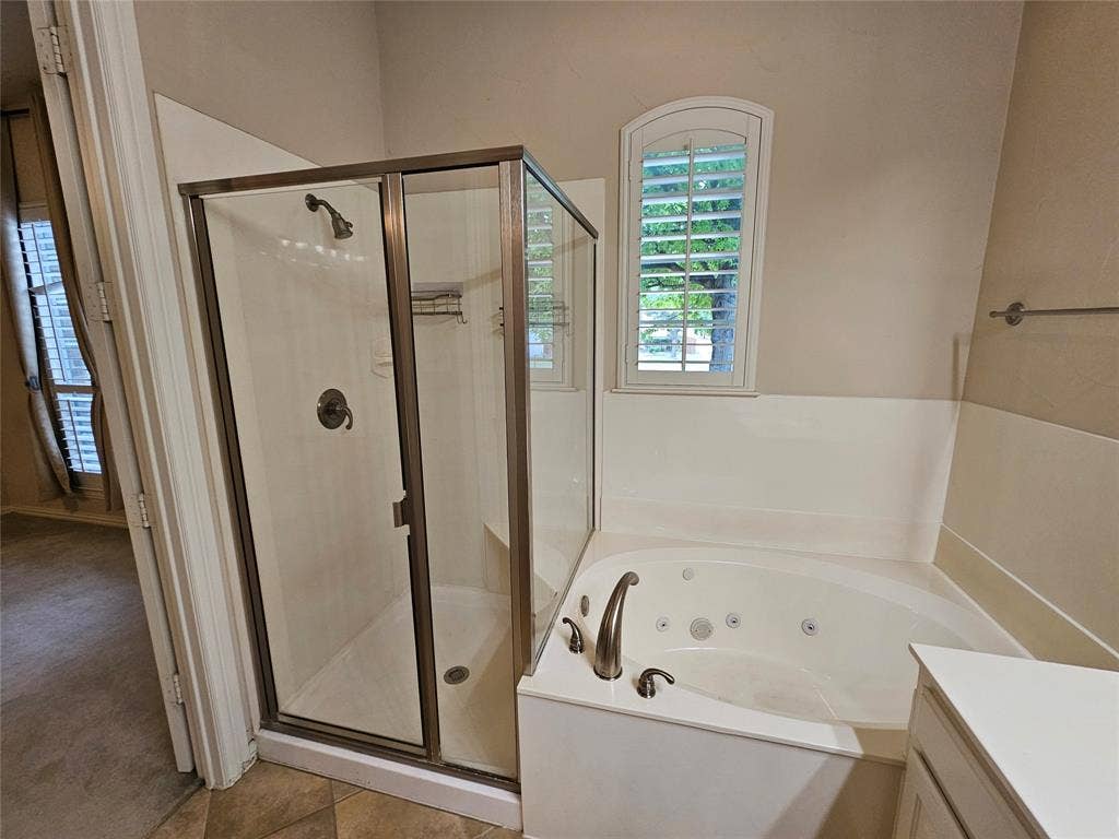 1009 Ricci Court, Irving, TX 75062 Dedicated shower enclosure with bronze-finish frame, jetted corner bathtub with deck-mounted fixtures, and an arched window featuring louvered shutters