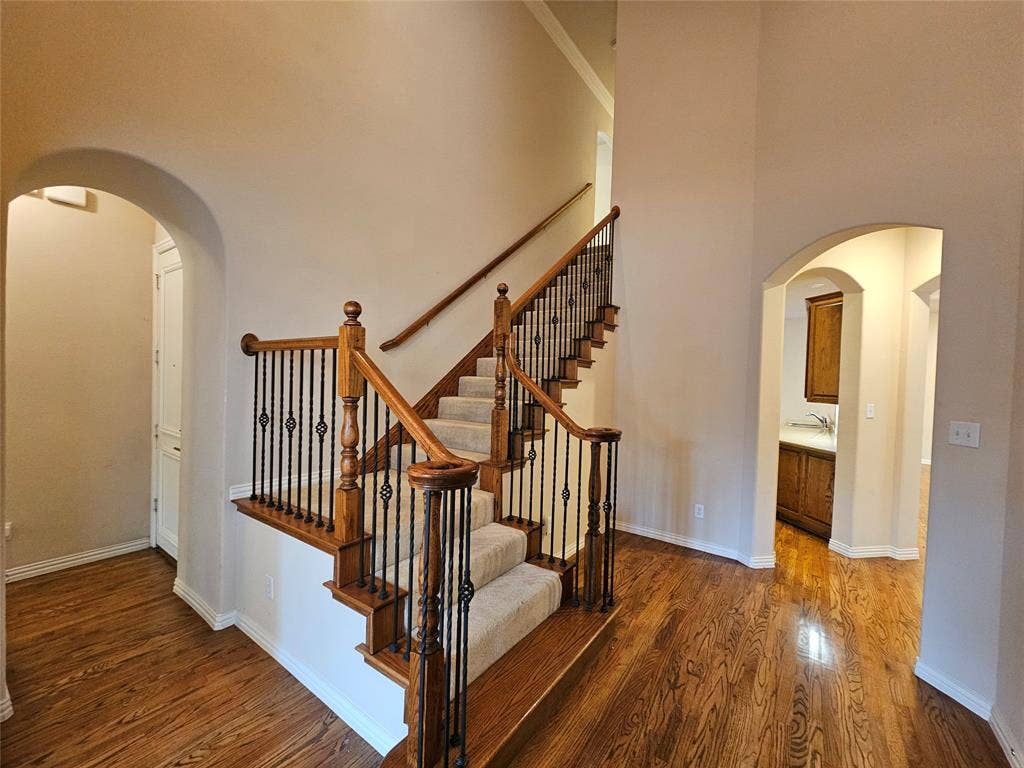 1009 Ricci Court, Irving, TX 75062 Elegant foyer showcasing a grand wooden staircase with turned balusters and a polished wood handrail, complemented by warm wood-finish flooring throughout