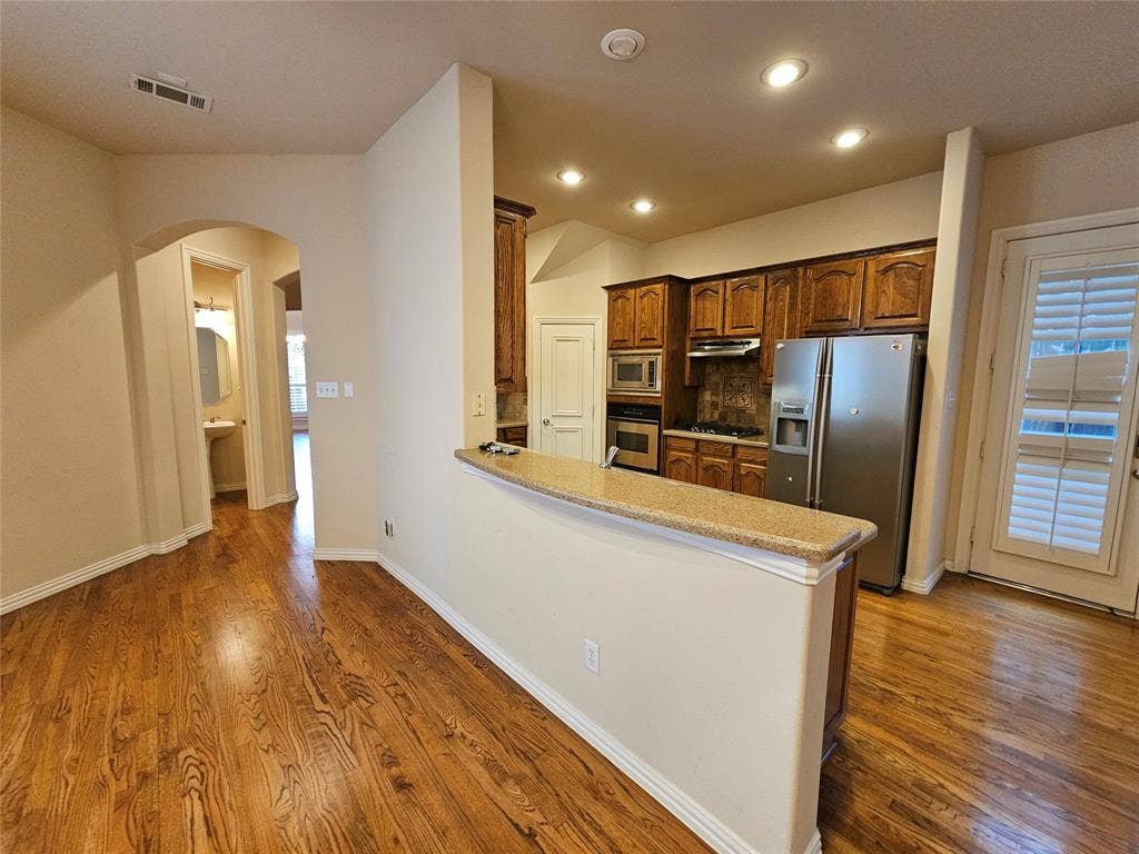 1009 Ricci Court, Irving, TX 75062 Wood-finish flooring throughout, kitchen with wood cabinetry, stainless steel appliances, and a granite-finish countertop peninsula