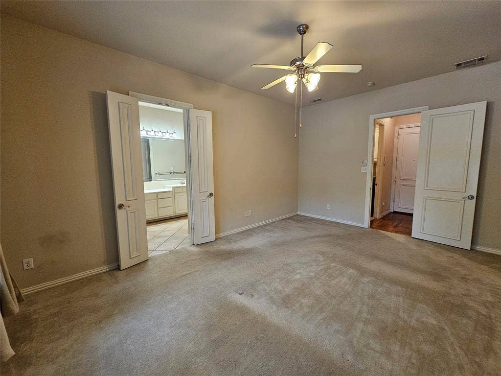 1009 Ricci Court, Irving, TX 75062 Carpeted interior space with a ceiling fan light fixture, offering access to an additional room through double doors, and a separate doorway to a hall with wood-finish flooring