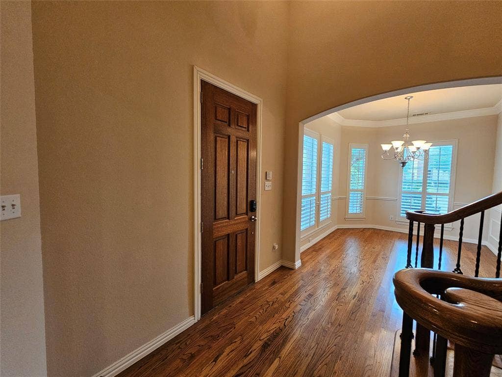 1009 Ricci Court, Irving, TX 75062 Wood-finish flooring, paneled entry door, arched doorway, chandelier, and a bay window with plantation shutters