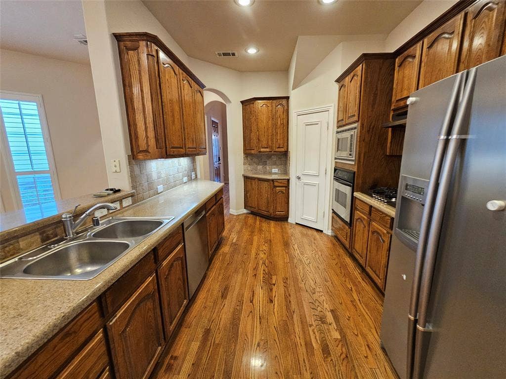 1009 Ricci Court, Irving, TX 75062 Kitchen featuring wood-finish flooring, ample wood cabinetry, light-toned countertops, and a tile backsplash