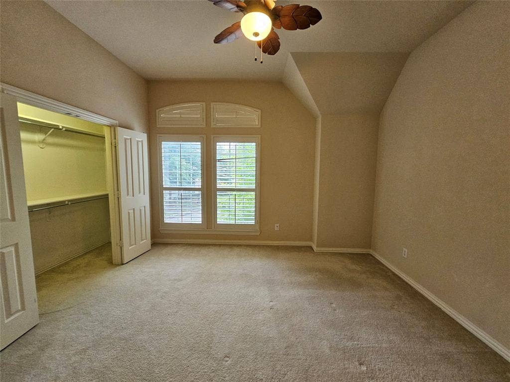 1009 Ricci Court, Irving, TX 75062 Arched transom window with plantation shutters, ceiling fan with light fixture, carpeted flooring, and a walk-in closet with double doors