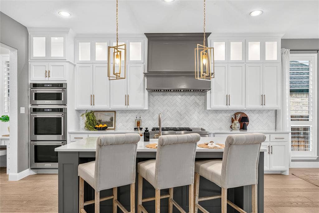 1581 Turnberry Drive, Prosper, TX 75078 Chef-inspired kitchen features a statement hood, gold pendant lighting, quartz countertops, floor to ceiling cabinets, double oven and gas cooktop.