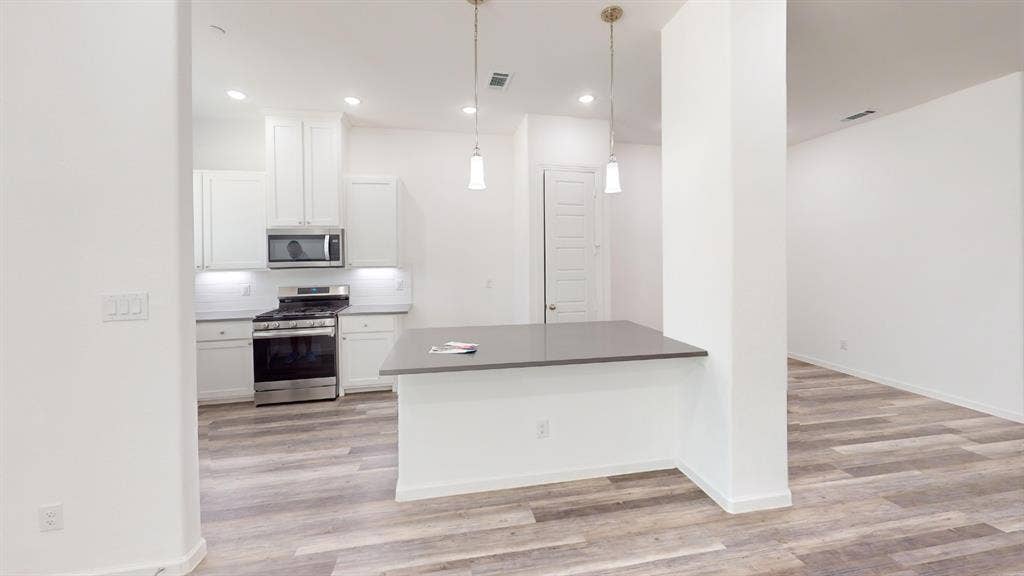 366 Buck Ridge Drive, Frisco, TX 75068 Modern kitchen featuring white cabinetry, stainless steel appliances, a dark countertop island, and wood-finish flooring