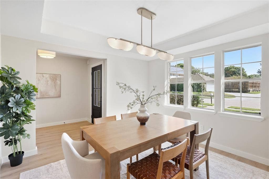 Recessed ceiling details, linear pendant light fixture, three large windows, wood-finish flooring, and a black paneled door