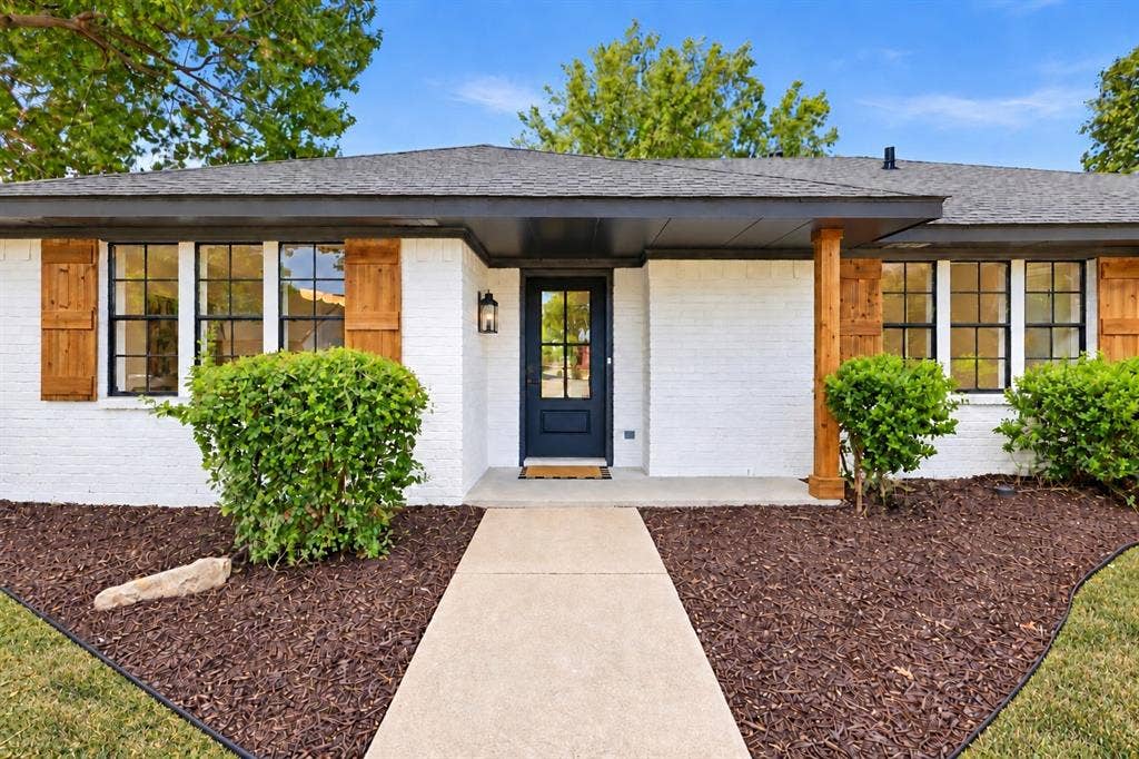 White brick exterior with a dark-paneled entry door, wood shutters, and a covered entryway