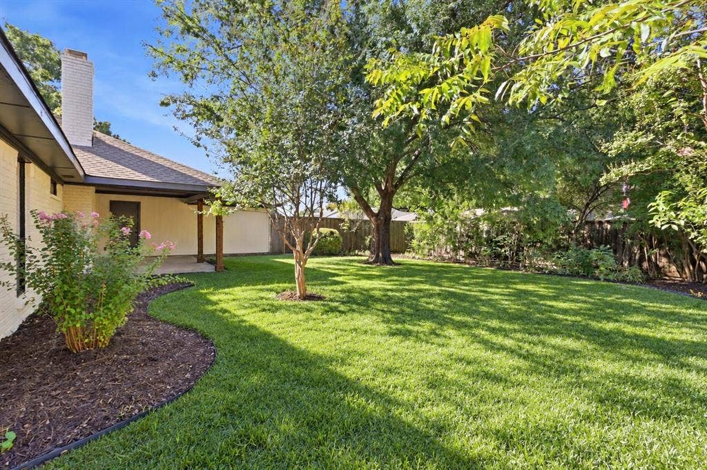 Expansive backyard featuring a manicured lawn, mature trees, and a covered patio with wood-wrapped columns