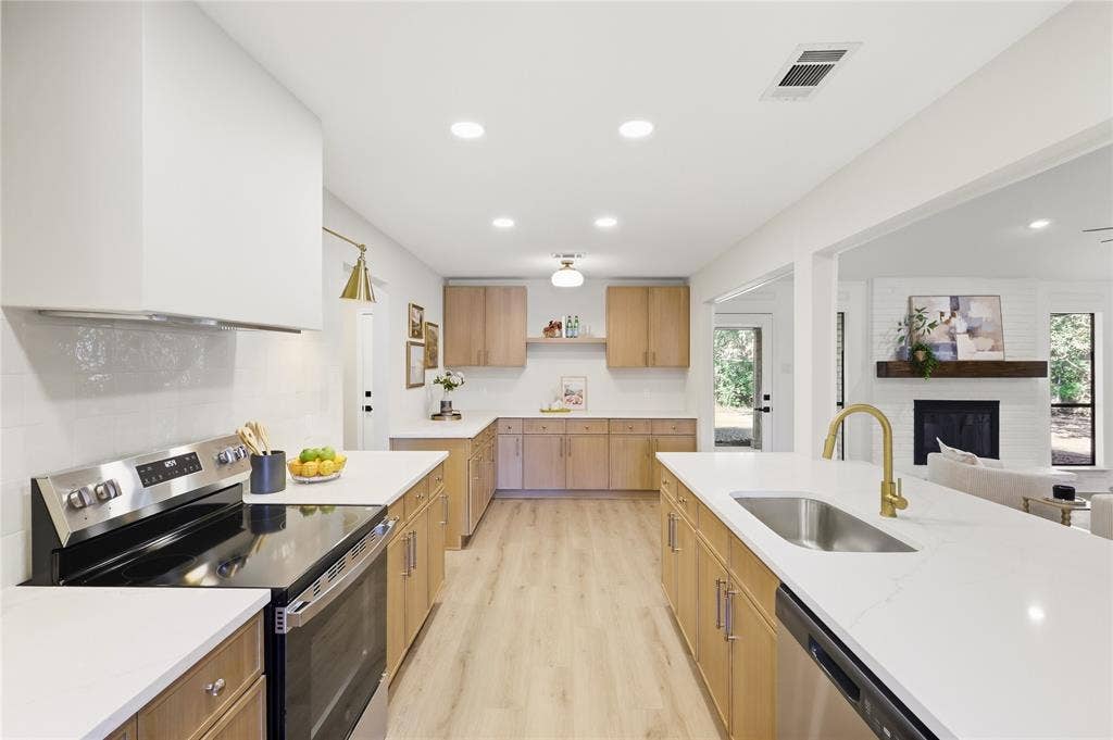 Modern kitchen with light wood-finish cabinetry, white countertops, stainless steel appliances, and wood-finish flooring