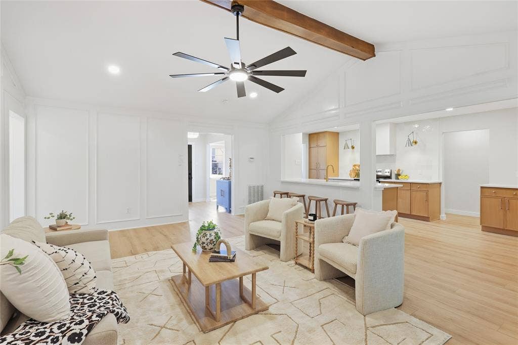 Vaulted ceiling with exposed wood beam, recessed lighting, wood-finish flooring, white paneling, and an open concept kitchen with light wood cabinetry