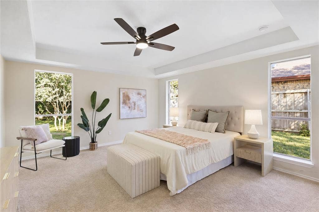 Recessed tray ceiling with crown molding, carpeted flooring, multiple rectangular windows, and a ceiling fan with integrated lighting
