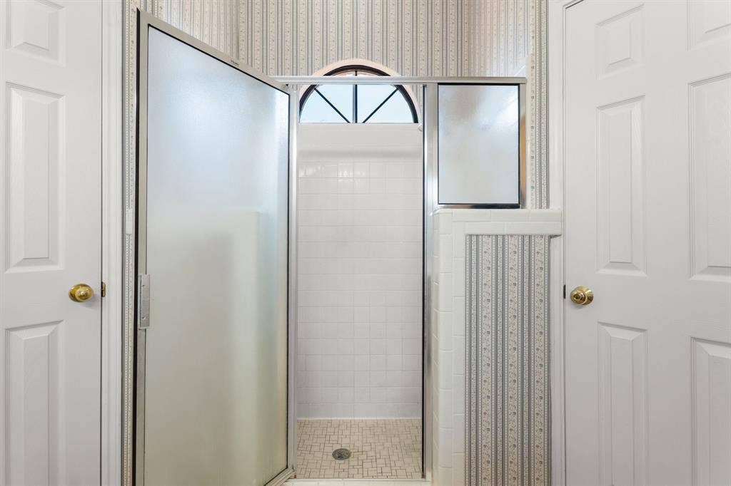 Shower enclosure with frosted glass door, white subway tile surround, tile mosaic shower pan, and arched transom window