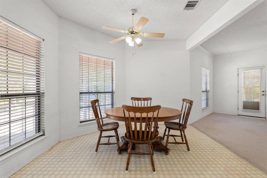 Vaulted ceiling with a ceiling fan, multiple windows with blinds, patterned flooring, and a glass-paneled door