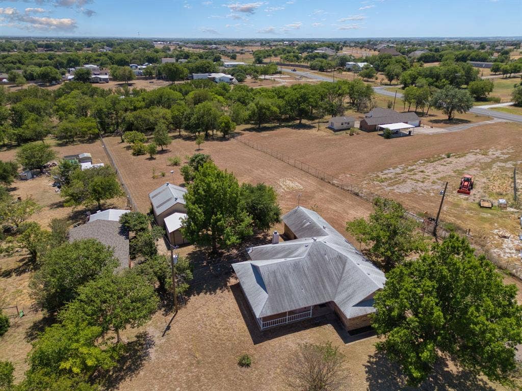 Expansive lot with mature trees, multiple outbuildings, and a main residence featuring a covered front porch and a multi-pitched roof