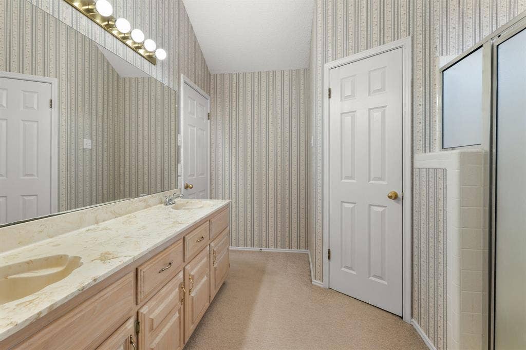 Dual-sink vanity with a light-toned countertop, extensive wall-mounted mirror, and overhead vanity lighting