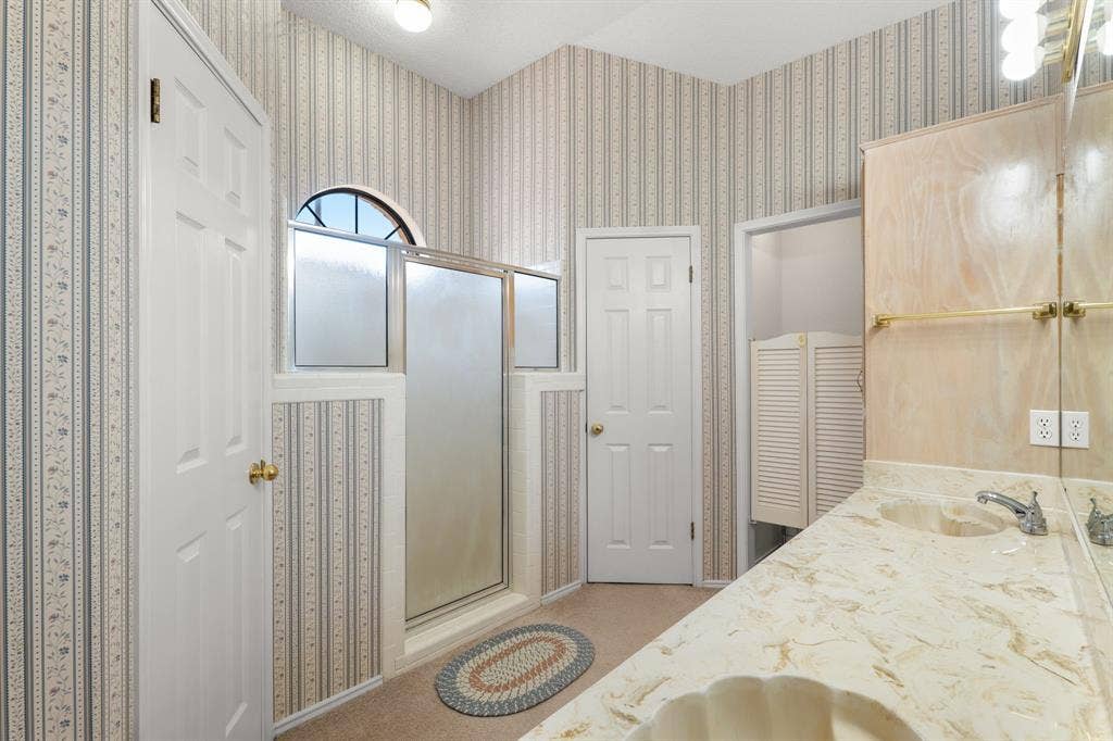 Dual vanity with integrated sinks, framed shower enclosure, arched window, and built-in cabinetry