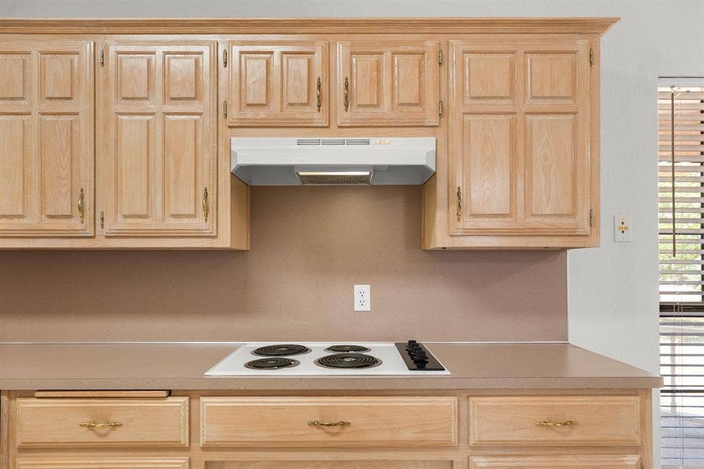 Warm wood cabinetry, integrated electric cooktop, and a matching range hood