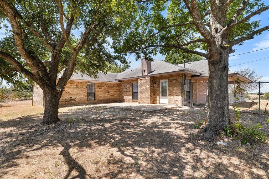 Brick exterior with covered patio, integrated chimney, and mature trees