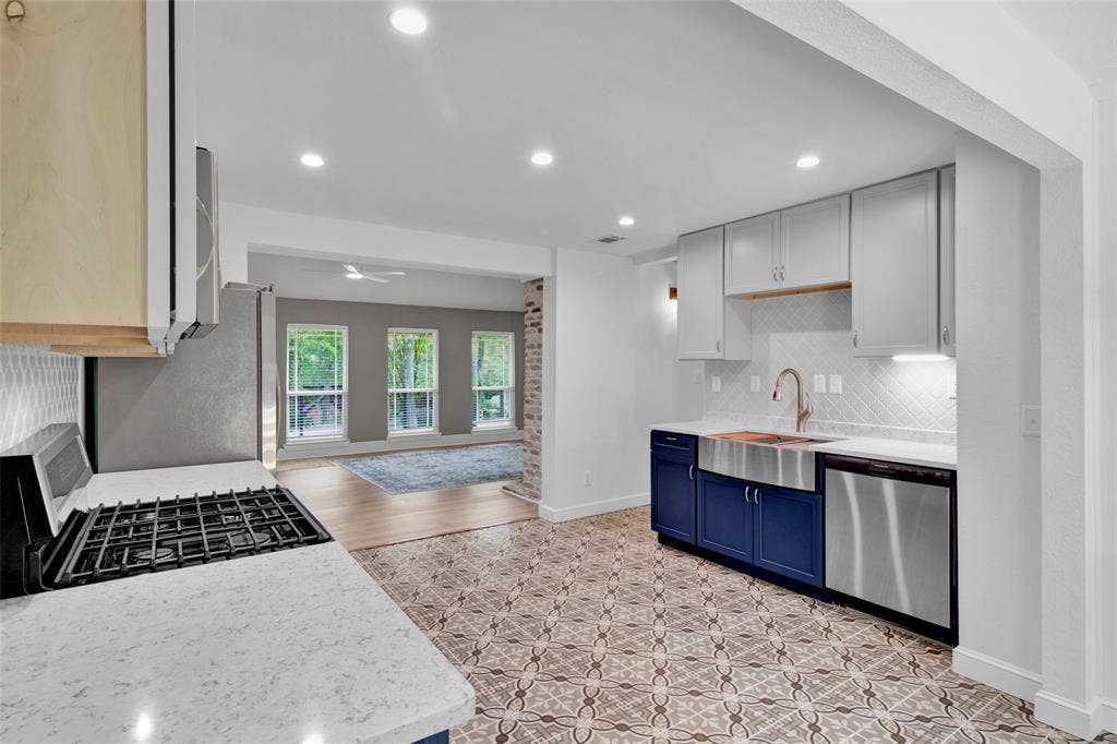 Kitchen with patterned tile flooring, light gray upper cabinetry, blue lower cabinetry, stainless steel farmhouse sink, and integrated stainless steel dishwasher