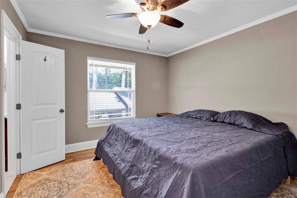 Wood-finish flooring, single window with blinds, ceiling fan with integrated lighting, and white trim work