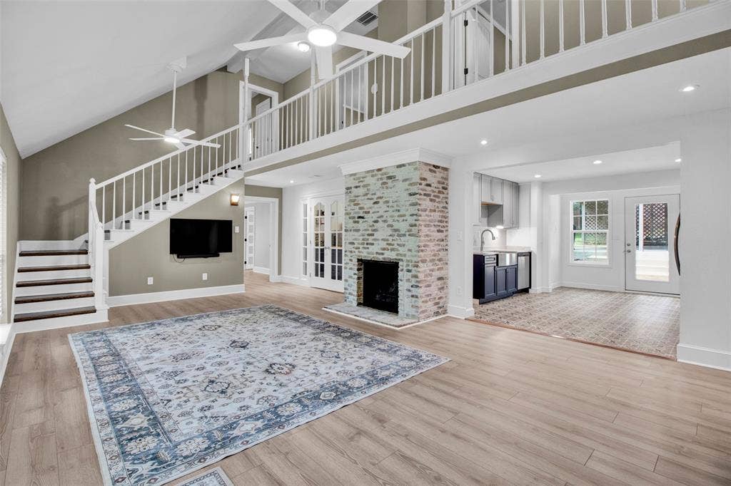 Vaulted ceilings with ceiling fans, light wood-finish flooring, white brick fireplace, wet bar with built-in cabinetry, and double French doors to the exterior