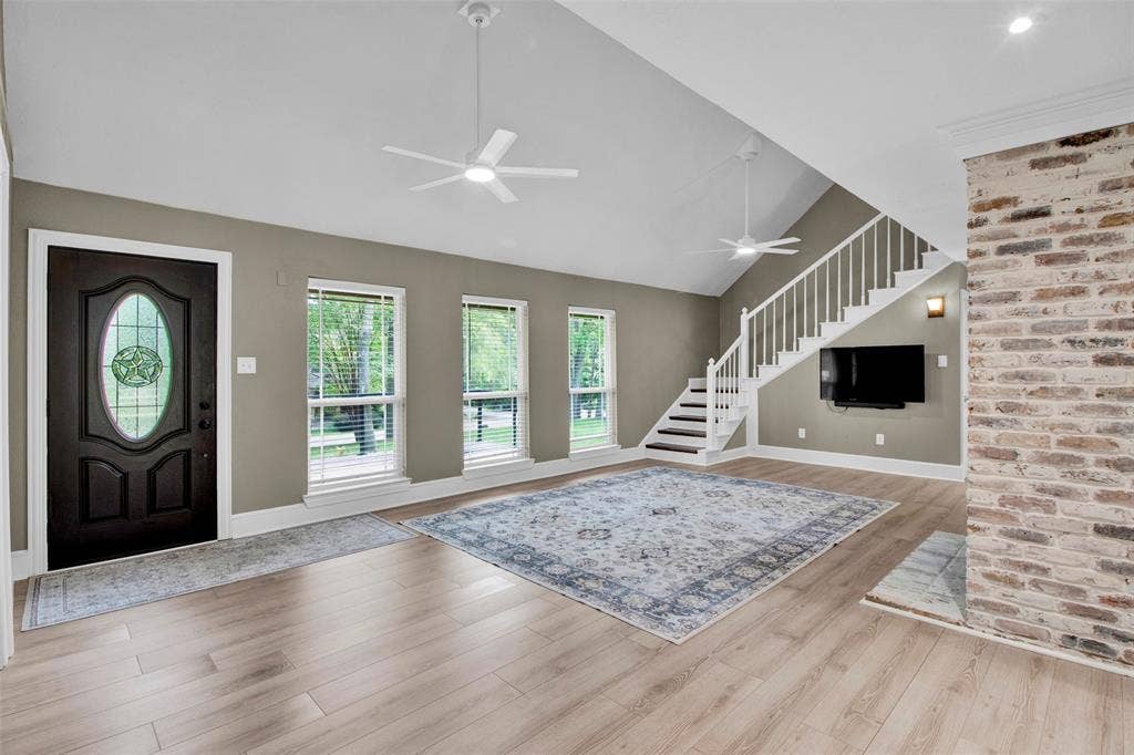 Vaulted ceilings, wood-finish flooring, staircase with white risers, decorative entry door, and brick accent wall